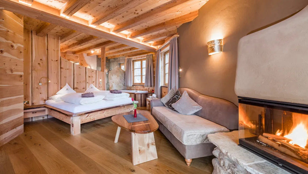 Suite in wood with sofa and fireplace of Naturhotel Lüsnerhof